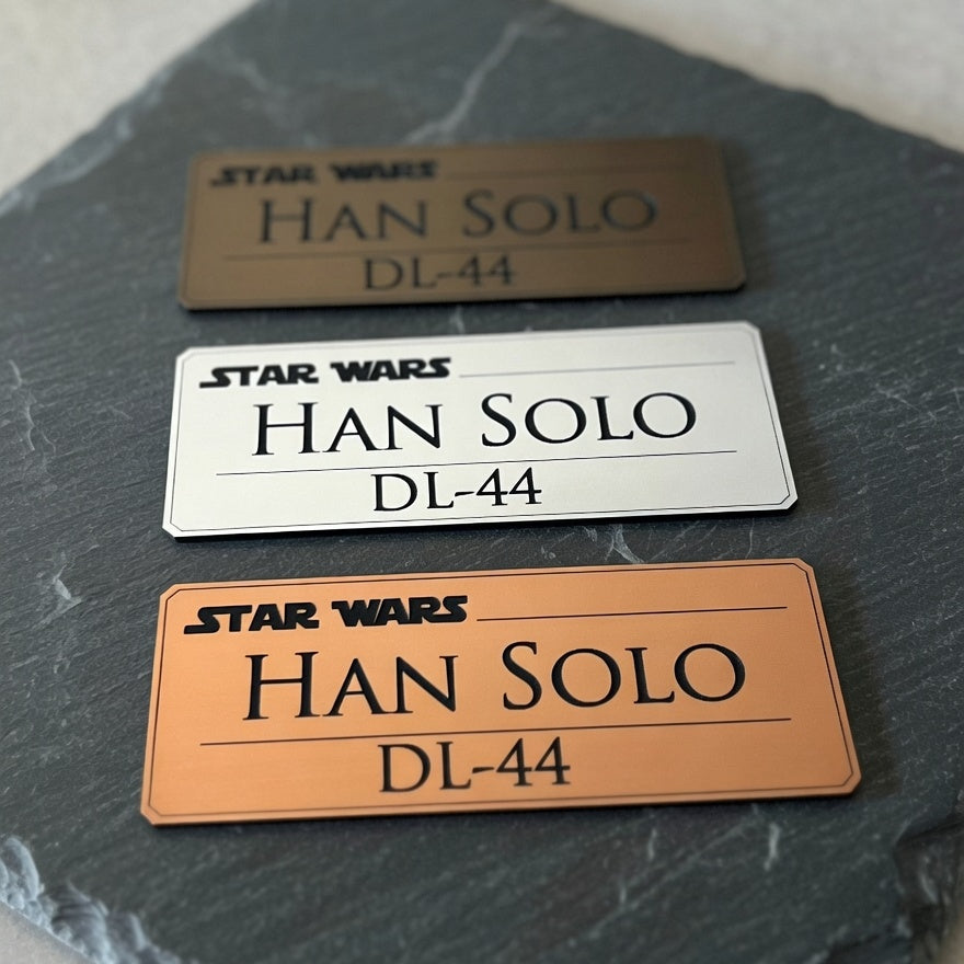 Three engraved Han Solo DL-44 display nameplates in silver, gold, and copper finishes, Outer Rim Props